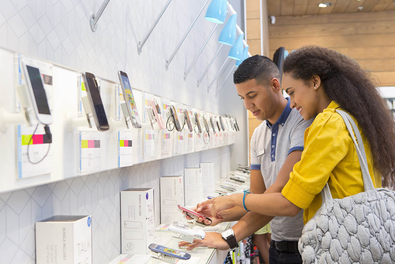 Woman talking to a salesperson in front of a wall displaying mobile phones